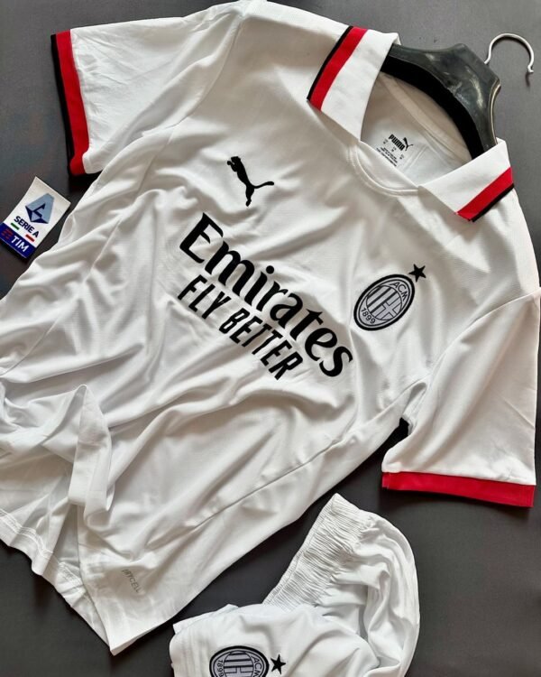 AC Milan 2024 Away Jersey (Player Version) displayed on a flat surface alongside matching shorts. This official away kit features a crisp white design with subtle vertical pinstripes, complemented by red and black accents on the collar and sleeve cuffs. The AC Milan crest and black Puma logo are prominently positioned on the chest, with the Emirates Fly Better sponsor logo in the center. Made from high-performance fabric, this jersey combines style with functionality, ideal for AC Milan fans and players.