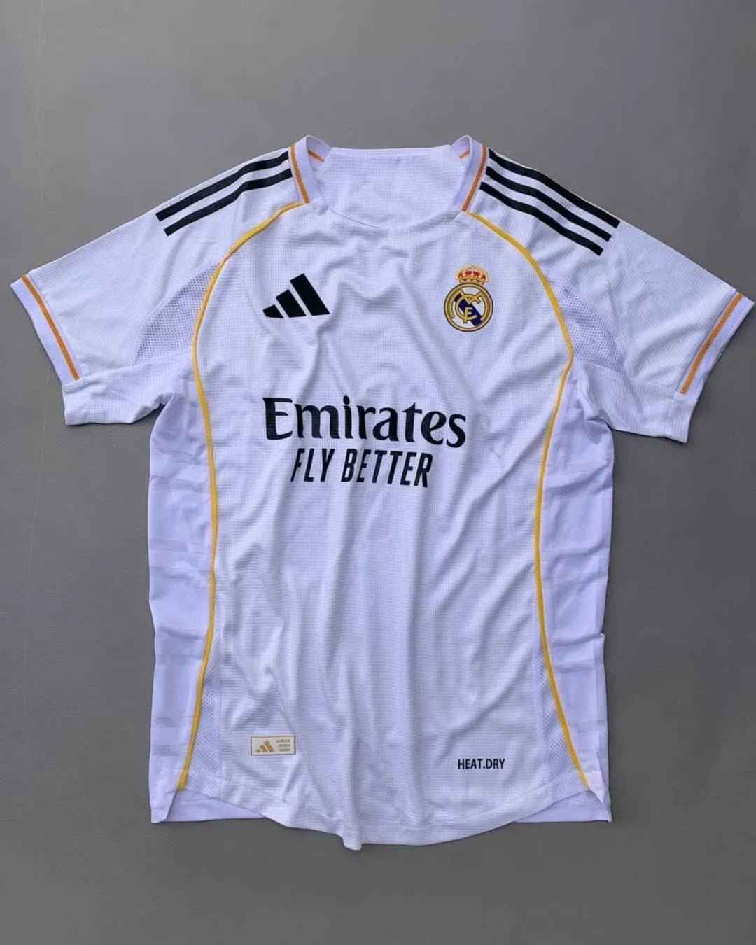 Real Madrid 2025/26 home jersey with classic white design, black adidas stripes, golden-yellow trim, Emirates Fly Better sponsor, and embroidered club crest – official fan and player kit